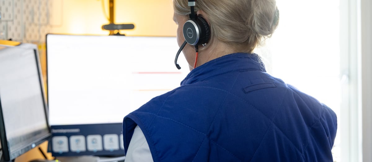 En kvinna med headset sitter framför en dator.