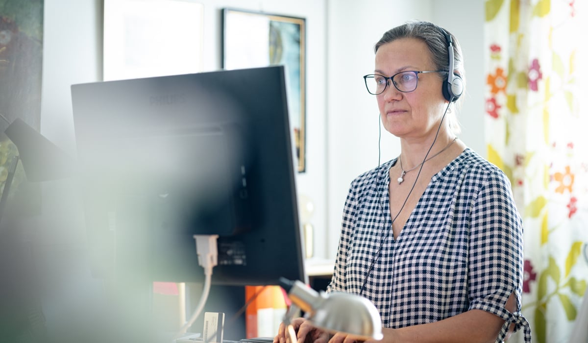 En kvinna med hörlurar på sig och använder en dator.